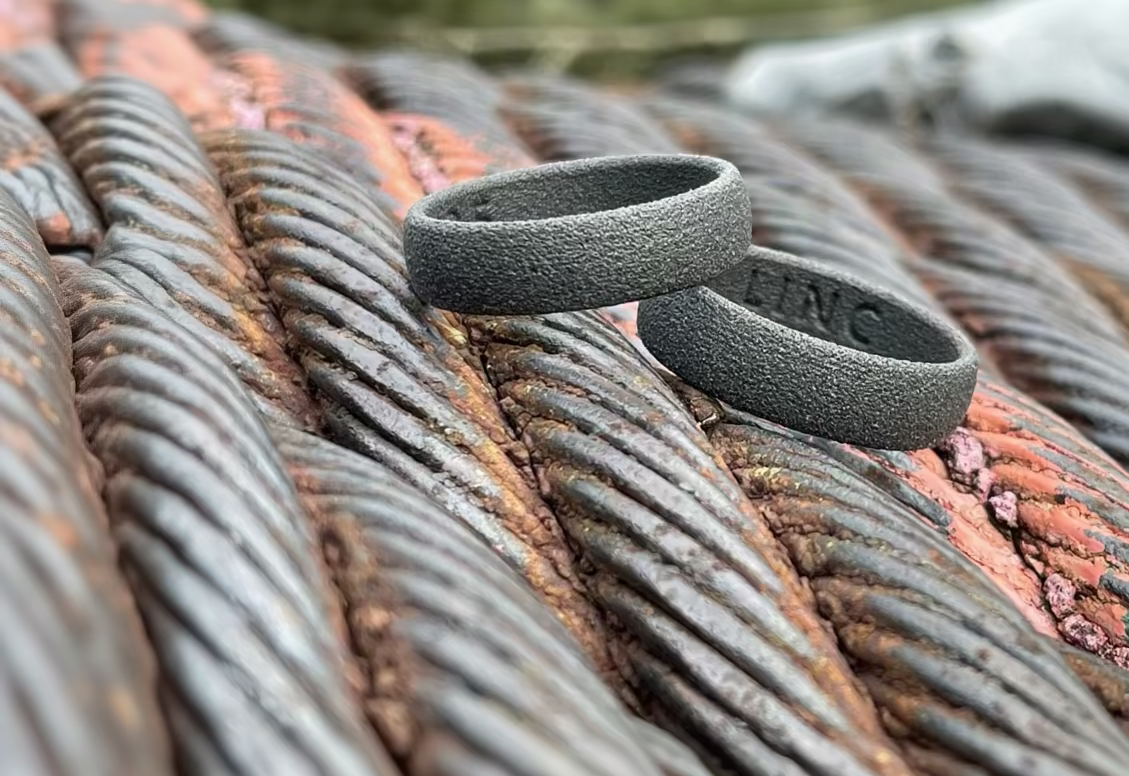 Two dark gray textured polymer ring bands resting on rusty metal cables outdoors.