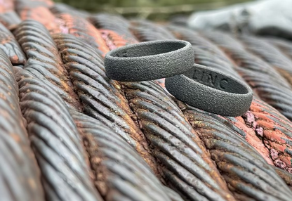 Two dark gray textured polymer ring bands resting on rusty metal cables outdoors.